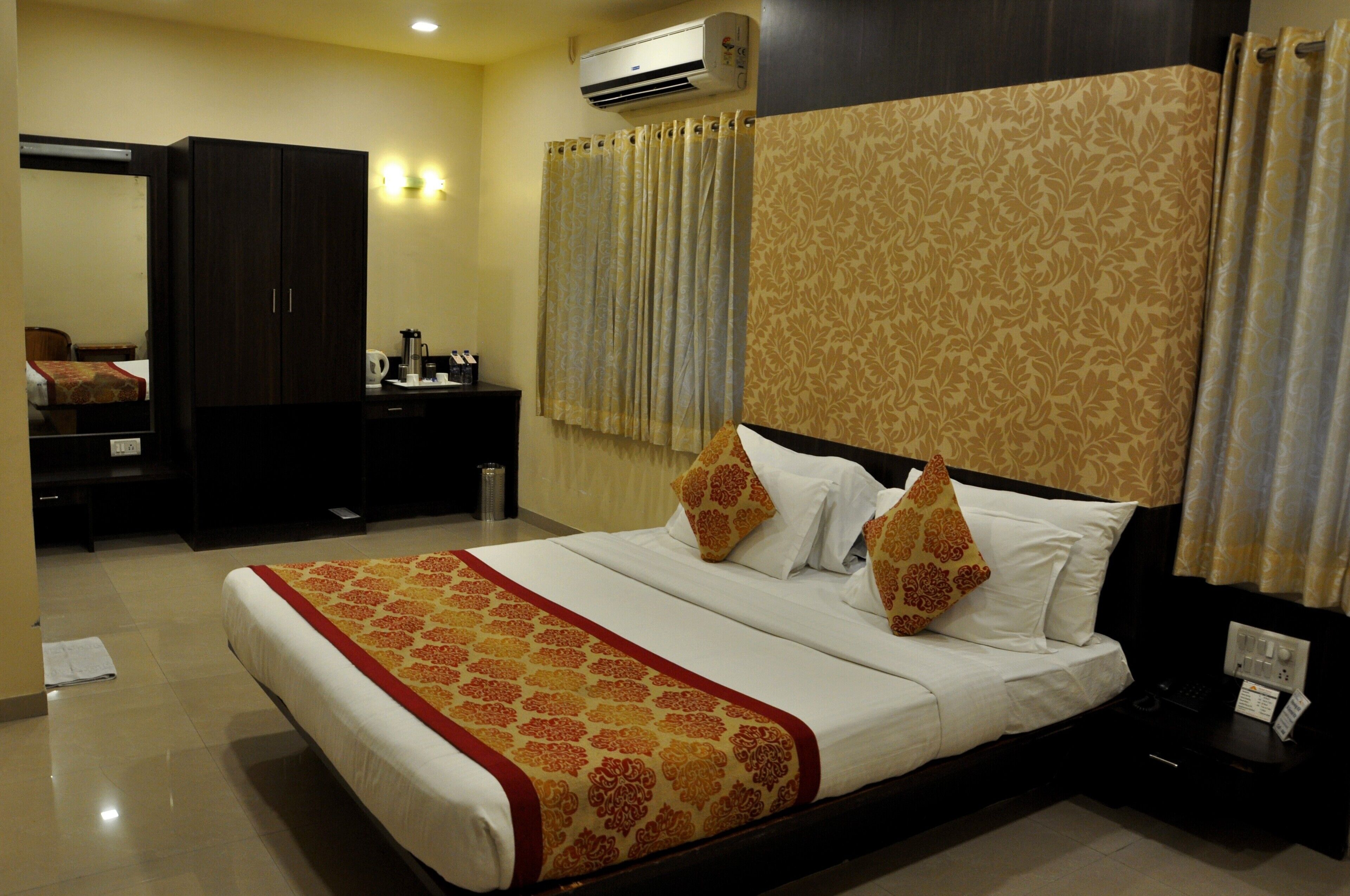 A hotel room with a large bed, a wardrobe, a desk, and a bathroom with curtains.