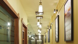 A hotel hallway with a wooden door, a glass wall, and a series of framed pictures on the wall. - Hotel Atria (Kolhapur)