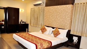 A hotel room with a large bed, a wooden wardrobe, a bedside table with a phone, and a wall-mounted air conditioner. - Hotel Atria (Kolhapur)
