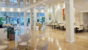 Un amplio vestíbulo de hotel con techos altos, ventanas grandes y un piso de mármol pulido.