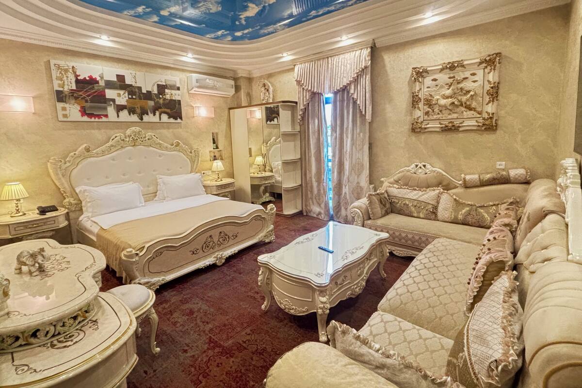Un dormitorio lujoso con una cama grande, un sofá, una mesa de centro de vidrio y decoración elaborada.