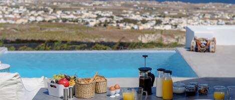 A breakfast setup with a view of a coastal town and a pool.