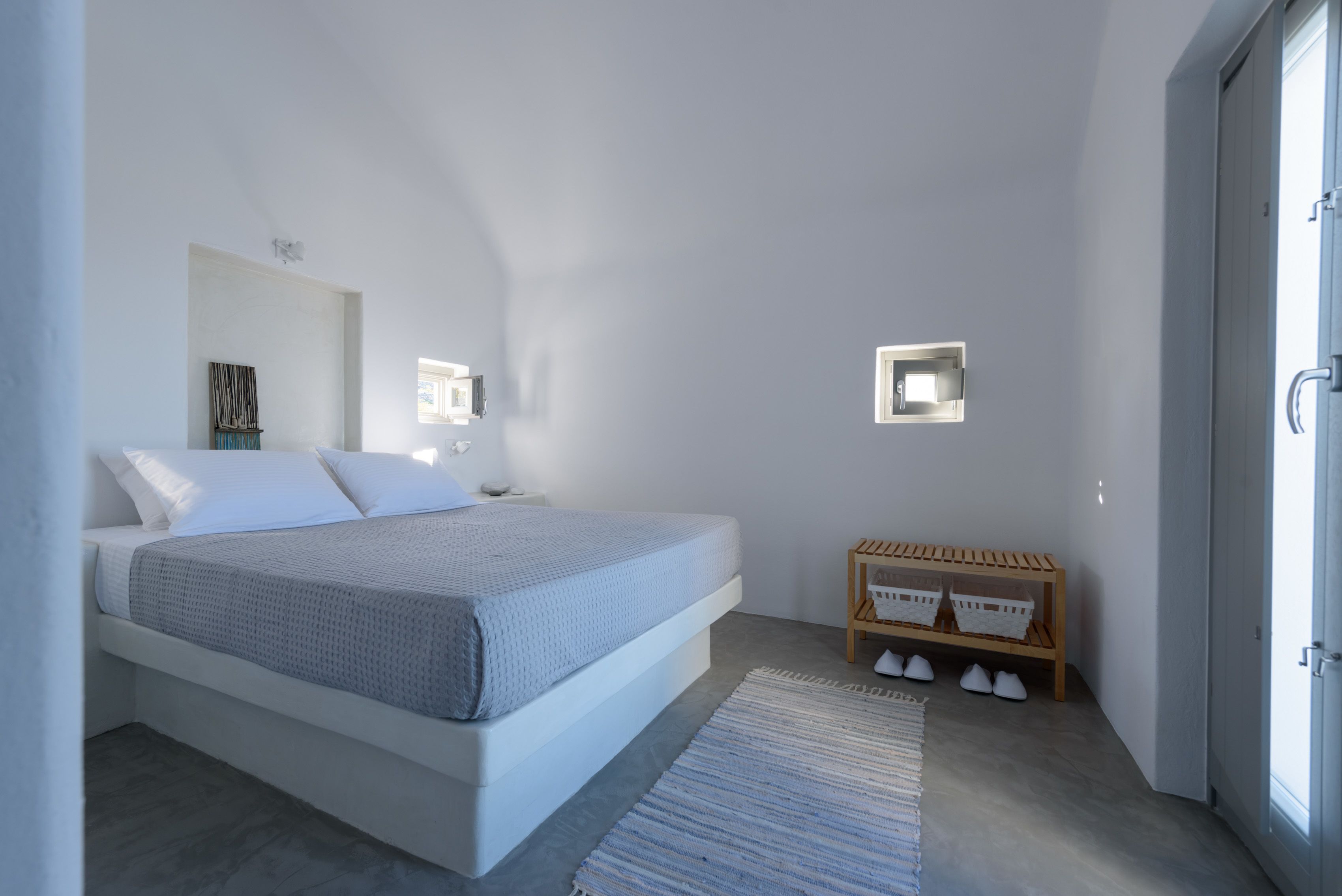 Une chambre à coucher moderne avec un grand lit, des tables de chevet, un banc avec des paniers et une vue sur l’extérieur.