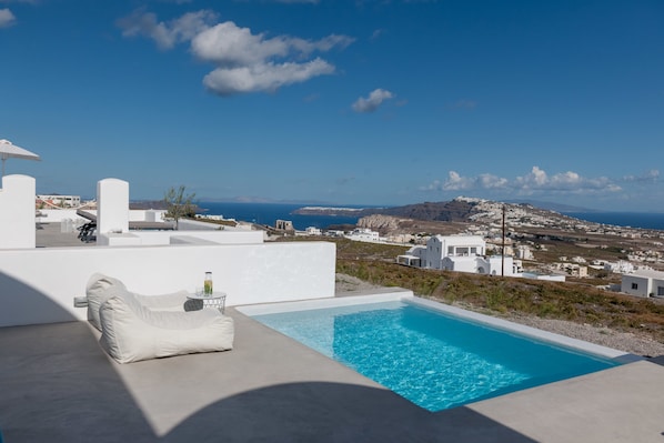 A modern outdoor pool area with a view of a coastal town and the sea.