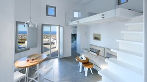 A modern, minimalist room with a dining area, a sofa, and a staircase. - Sandy & Salty Villas (Santorini)