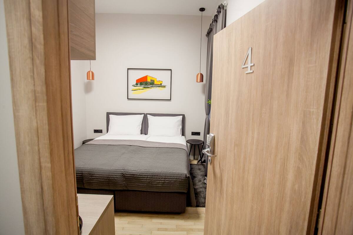 A bedroom with a bed, a bedside table, a chair, a wardrobe, and a framed picture on the wall.