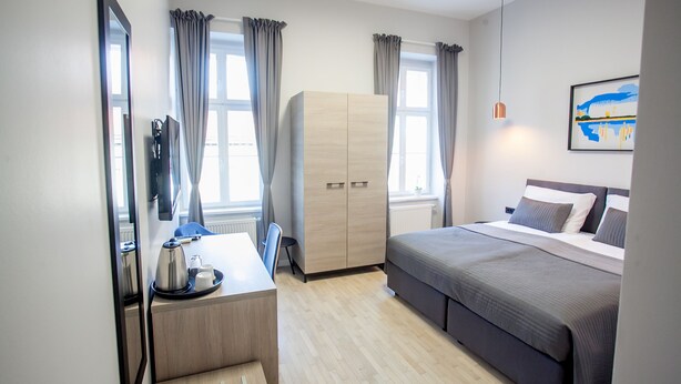 A modern hotel room with a bed, a desk with a chair, a wardrobe, and a large mirror. - Zagreb City Vibe Apartments & Rooms (Zagreb)