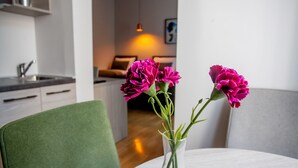 A dining table with a vase of pink flowers, a green chair, and a kitchen area in the background. - Zagreb City Vibe Apartments & Rooms (Zagreb)