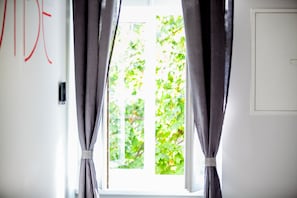 A window with curtains, a white door, and a view of green foliage outside. - Zagreb City Vibe Apartments & Rooms (Zagreb)