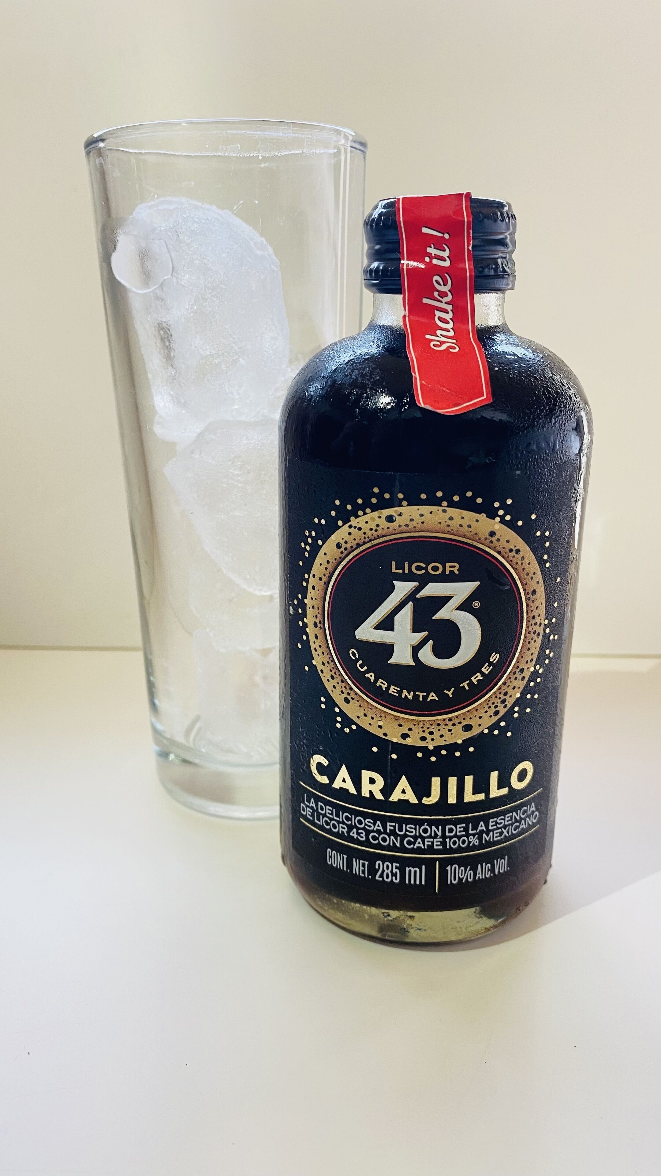 Una botella de licor Carajillo junto a un vaso lleno de hielo.