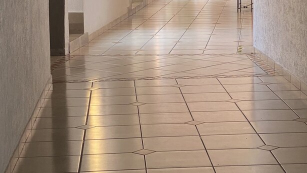 A long, narrow hallway with tiled flooring, a potted plant, and a staircase at the end. - Hotel Bahia (Guadalajara)