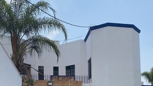 A building with a white and blue facade, a paved entrance, and a palm tree. - Hotel Bahia (Guadalajara)