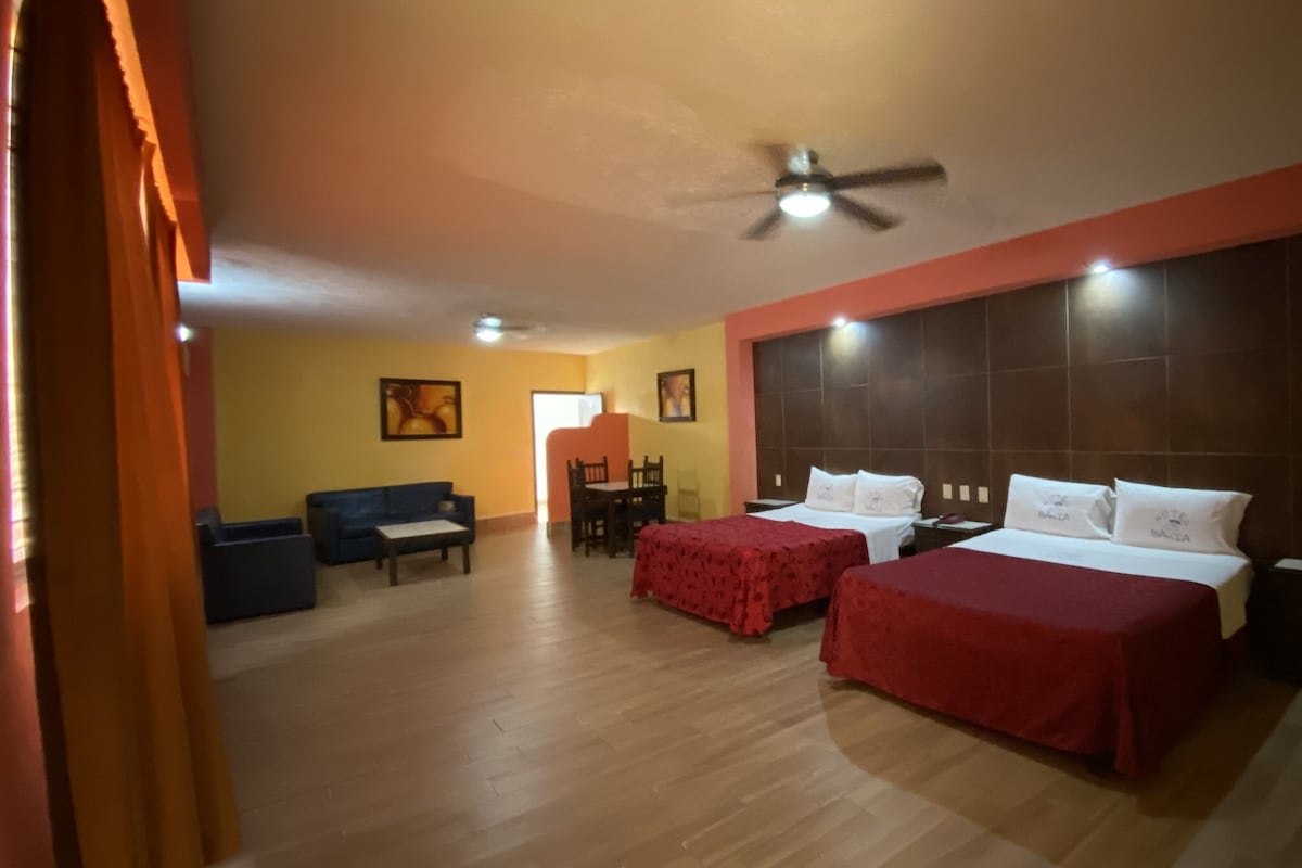 Habitación de hotel con dos camas, ventilador de techo, zona de comedor y sofá.