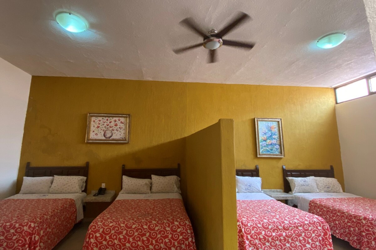 Una habitación de hotel con cuatro camas, un ventilador de techo y dos luces de techo.