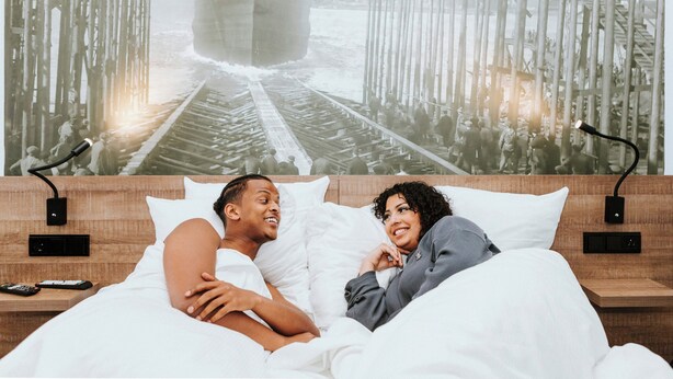 A bedroom with a large bed, a nightstand, and a wall-mounted lamp. - Rotterdam Teleport Hotel (Rotterdam)