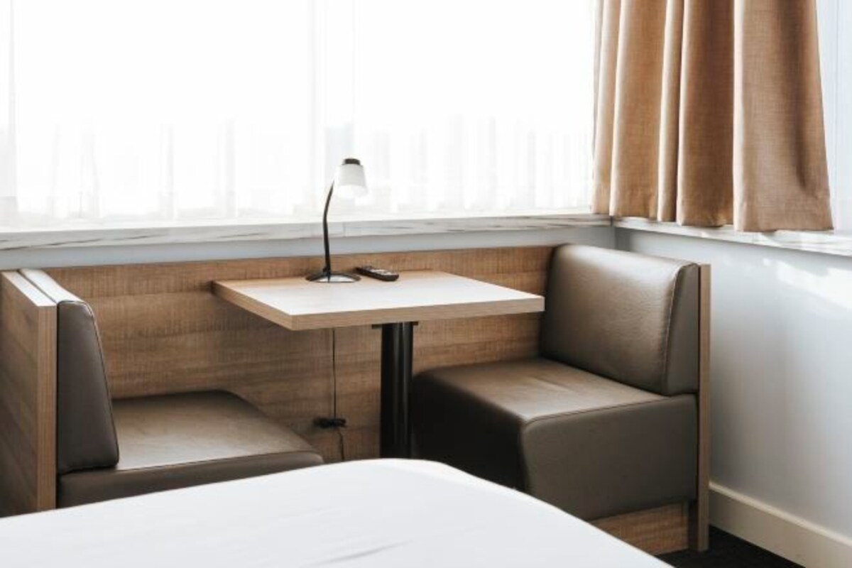 A hotel room with a bed, a small table with a lamp, and two chairs.