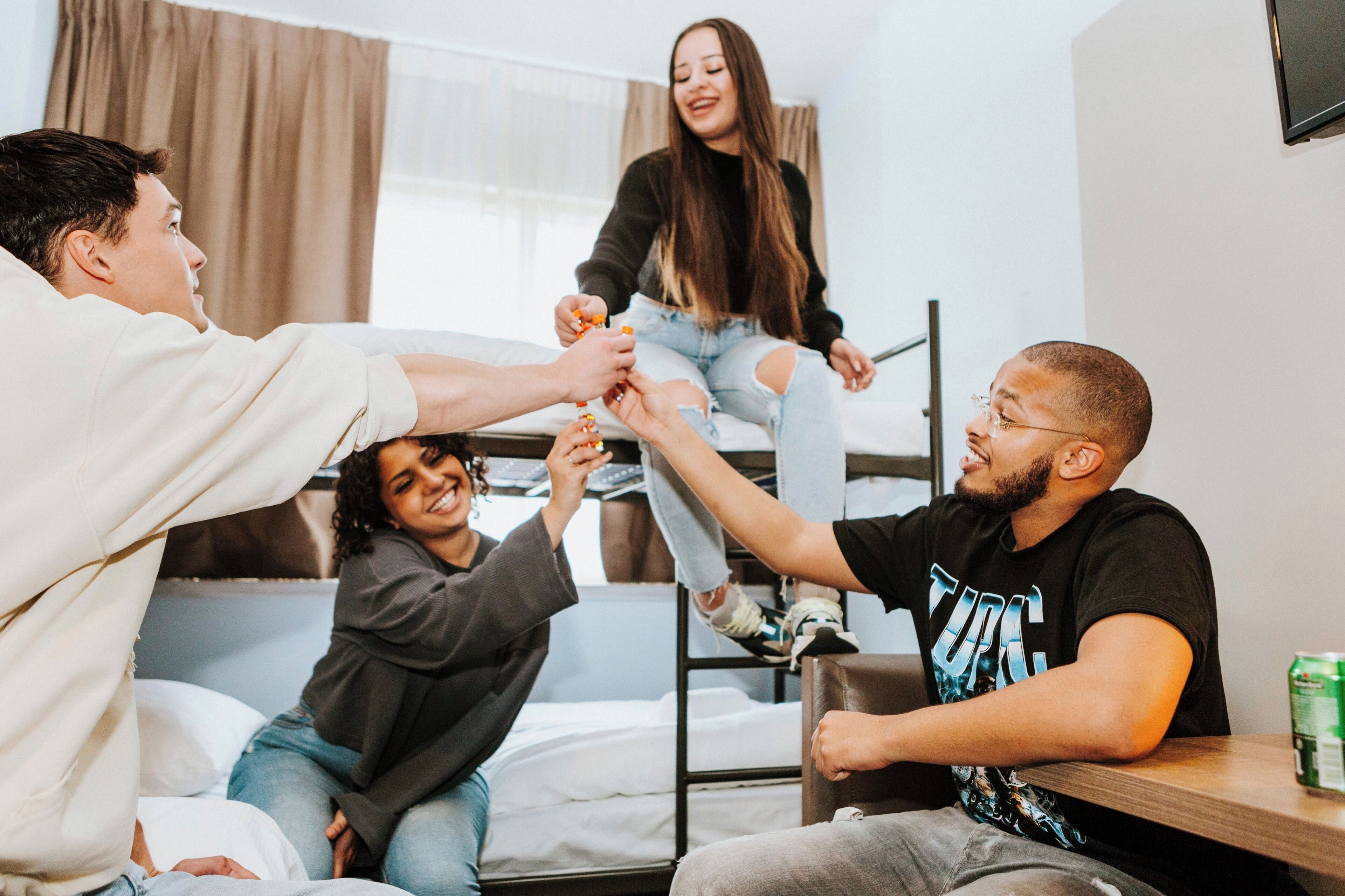 Eine Gruppe von Menschen in einem Schlafsaal mit Etagenbetten, einem Holztisch und einem Fernseher an der Wand.