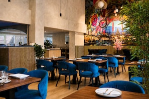 A restaurant interior with blue upholstered chairs, wooden tables, and a colorful mural on the wall. - Rotterdam Teleport Hotel (Rotterdam)