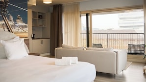 A modern hotel room with a large bed, a sofa, a kitchenette, and a balcony with a city view. - Rotterdam Teleport Hotel (Rotterdam)