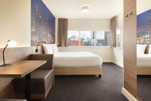 Habitación de hotel con cama, escritorio y vistas a la ciudad a través de amplias ventanas.