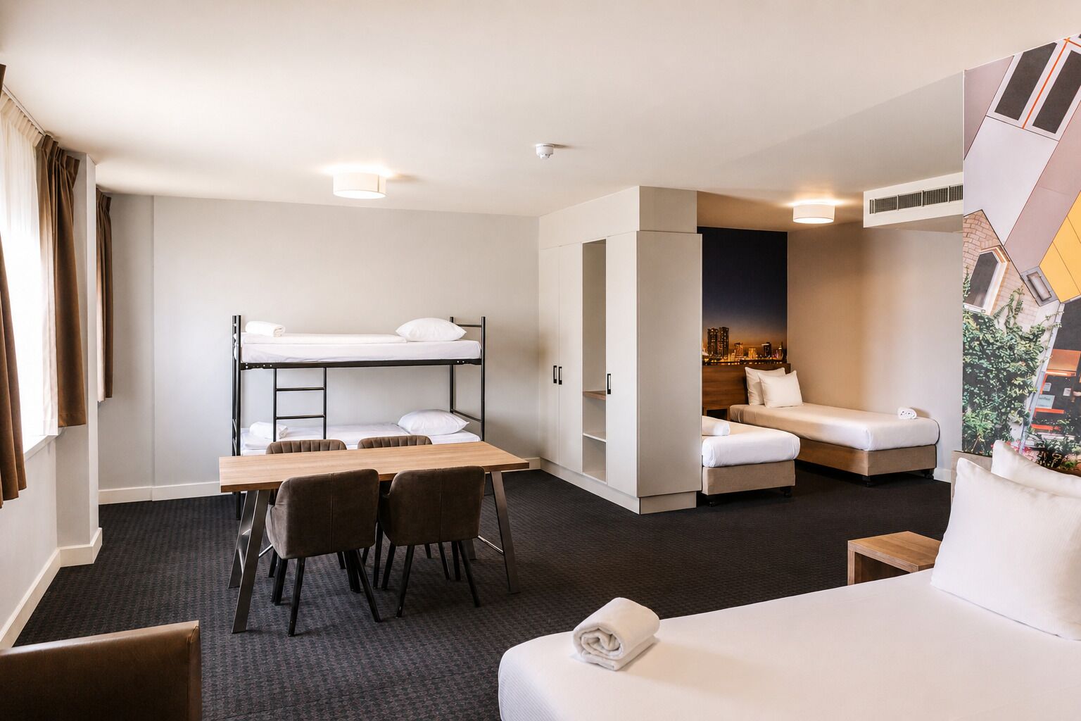 Une chambre d’hôtel avec un lit superposé, un bureau avec des chaises, un canapé et un lit.