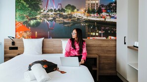 A hotel room with a bed, a laptop, and a large cityscape mural on the wall. - Rotterdam Teleport Hotel (Rotterdam)