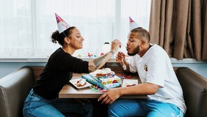 Two people sitting at a table with a birthday cake and party hats, in a room with a window and curtains. - Rotterdam Teleport Hotel (Rotterdam)