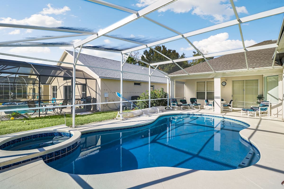 Ein Schwimmbecken mit Sonnensegel, Liegestühlen und einer überdachten Terrasse.