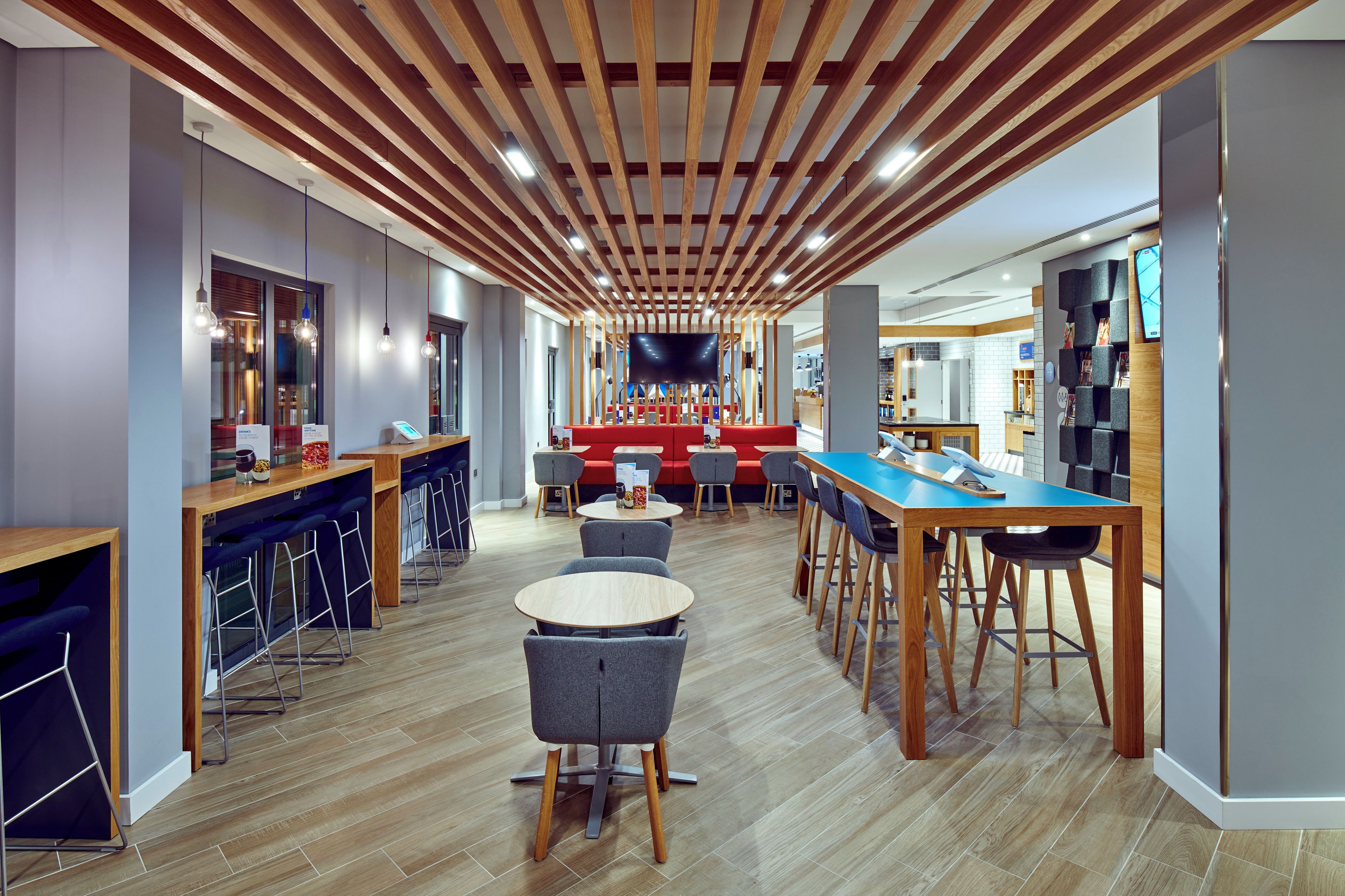 Un espace bar moderne avec des poutres en bois au plafond, des tabourets de bar et des tables rondes.