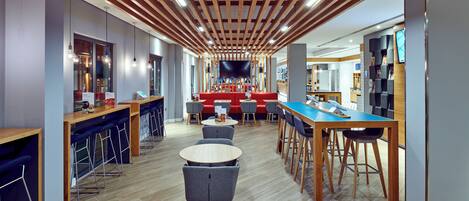 A modern bar area with wooden ceiling beams, bar stools, and round tables.