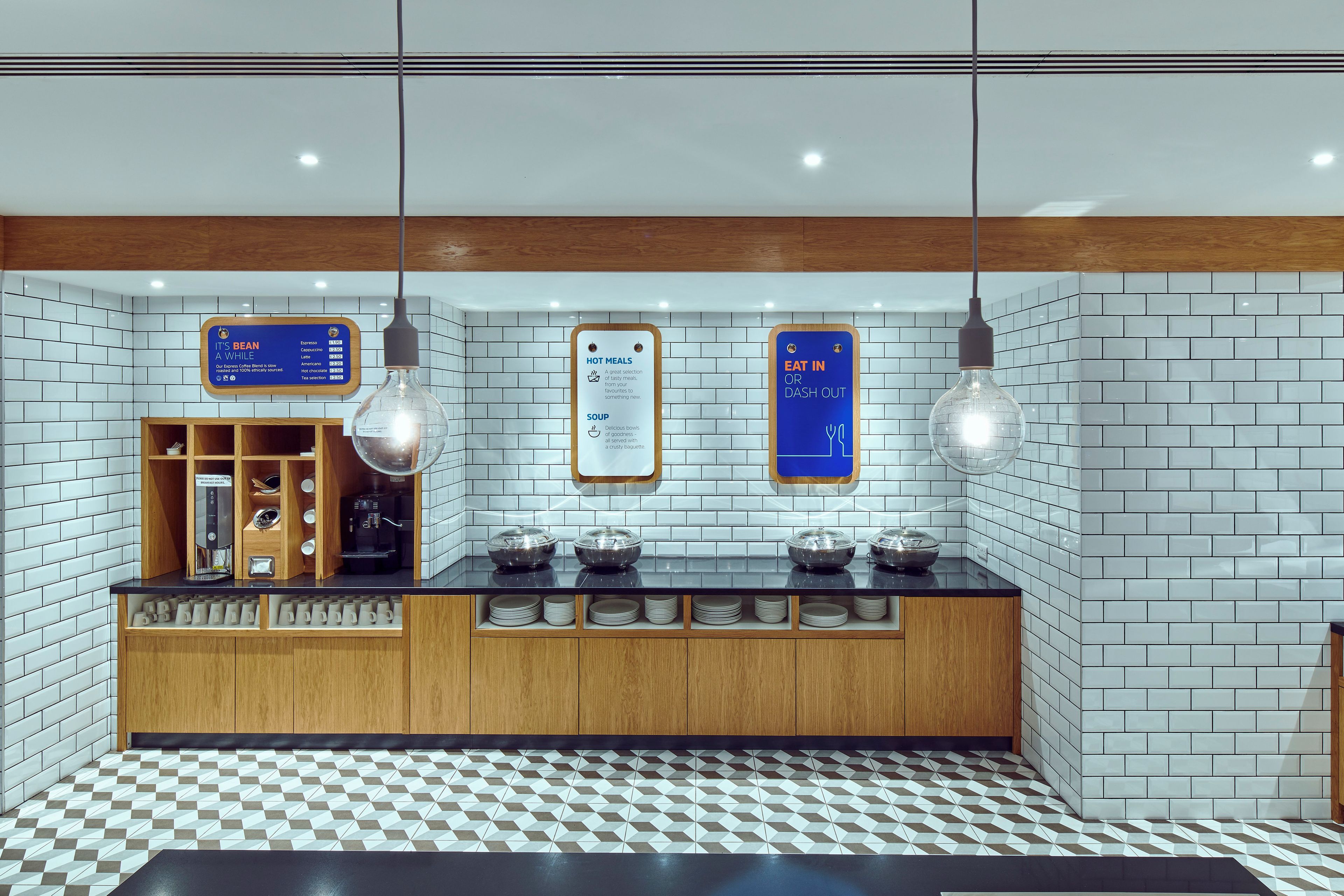 Un área de cocina moderna con una estación de café, una pizarra de menú y un letrero que indica comidas calientes o servicio de restaurante.