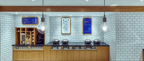 Un espace cuisine moderne comprenant un coin café, un tableau affichant le menu et un panneau indiquant les plats chauds ou les options de restauration sur place.
