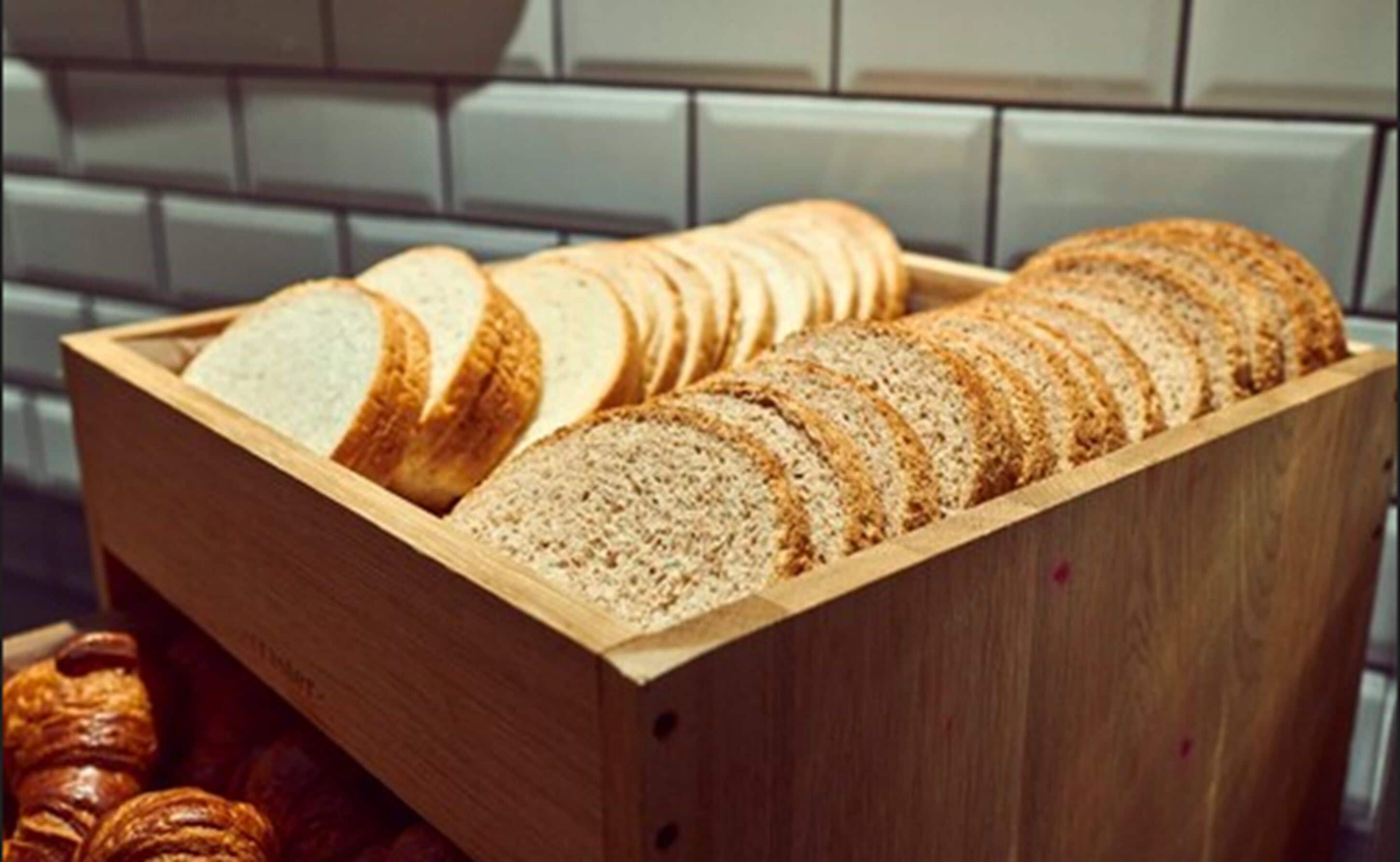 Una caja de madera con pan en rebanadas y croissants.