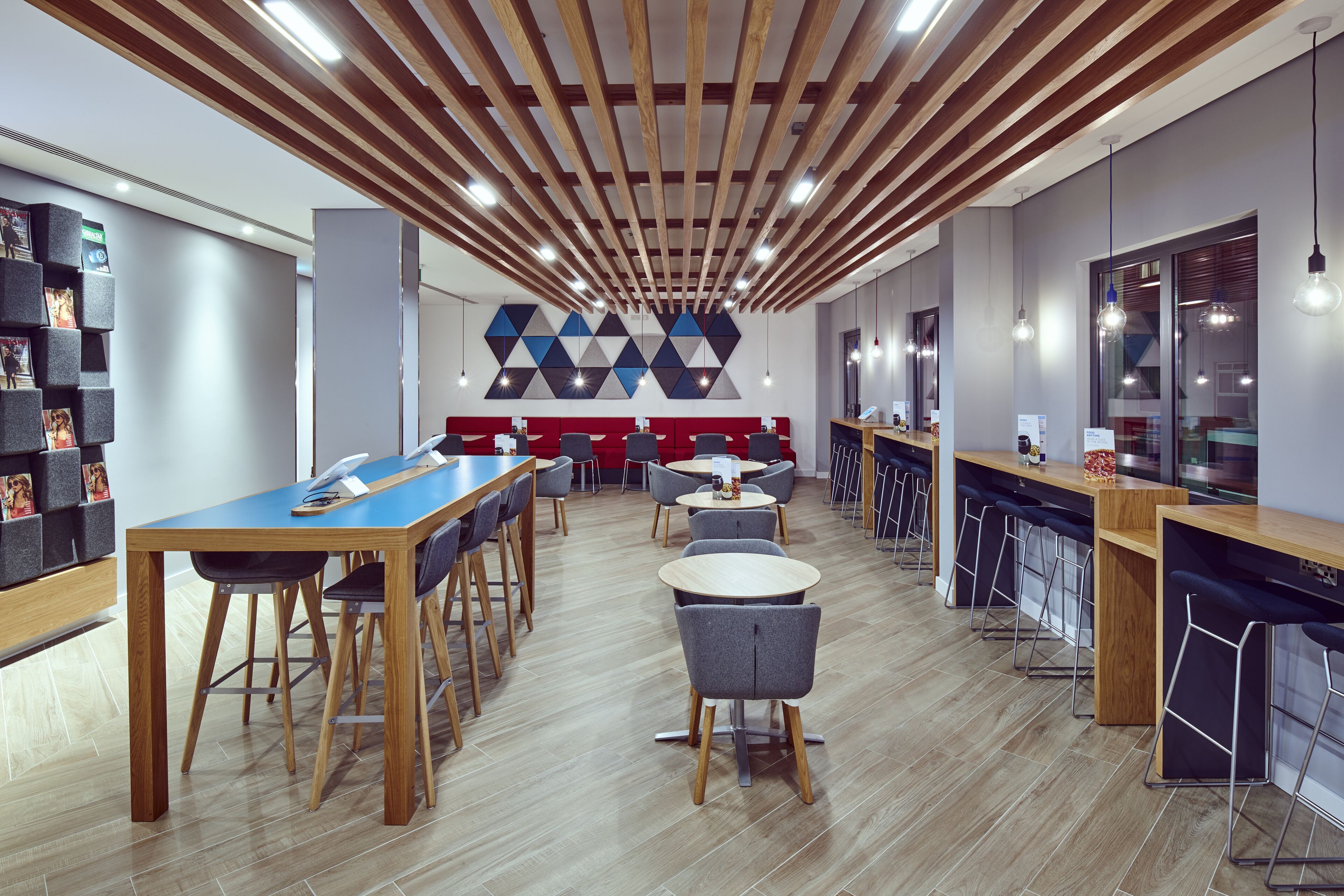 A modern restaurant with wooden ceiling beams, multiple tables and chairs, and a bar area.