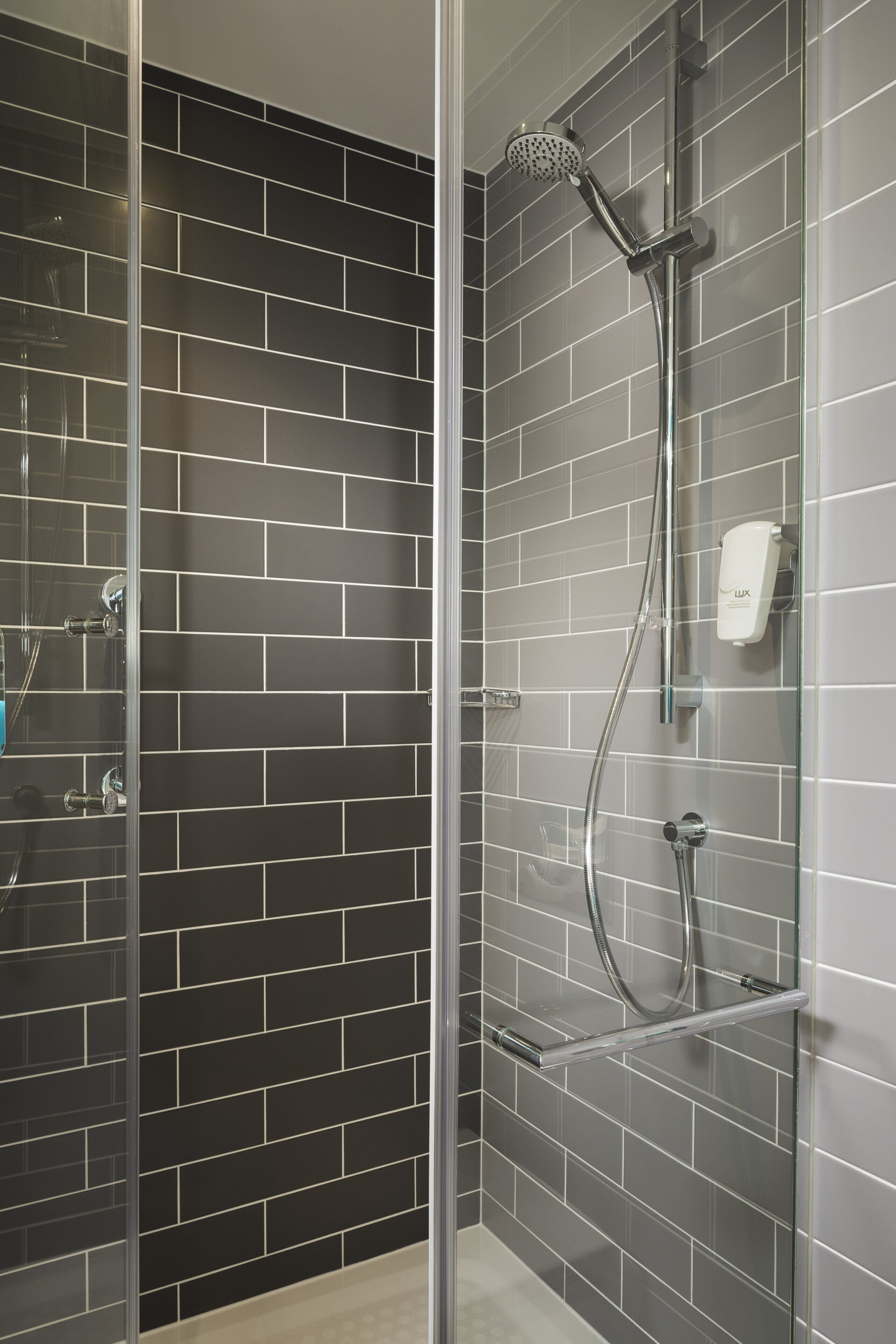 Een moderne douchecabine met een glazen deur, een handdouche en een extra douchetuit.