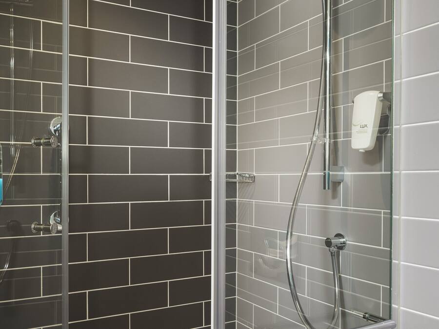 Een moderne douchecabine met een glazen deur, een handdouche en een extra douchetuit.
