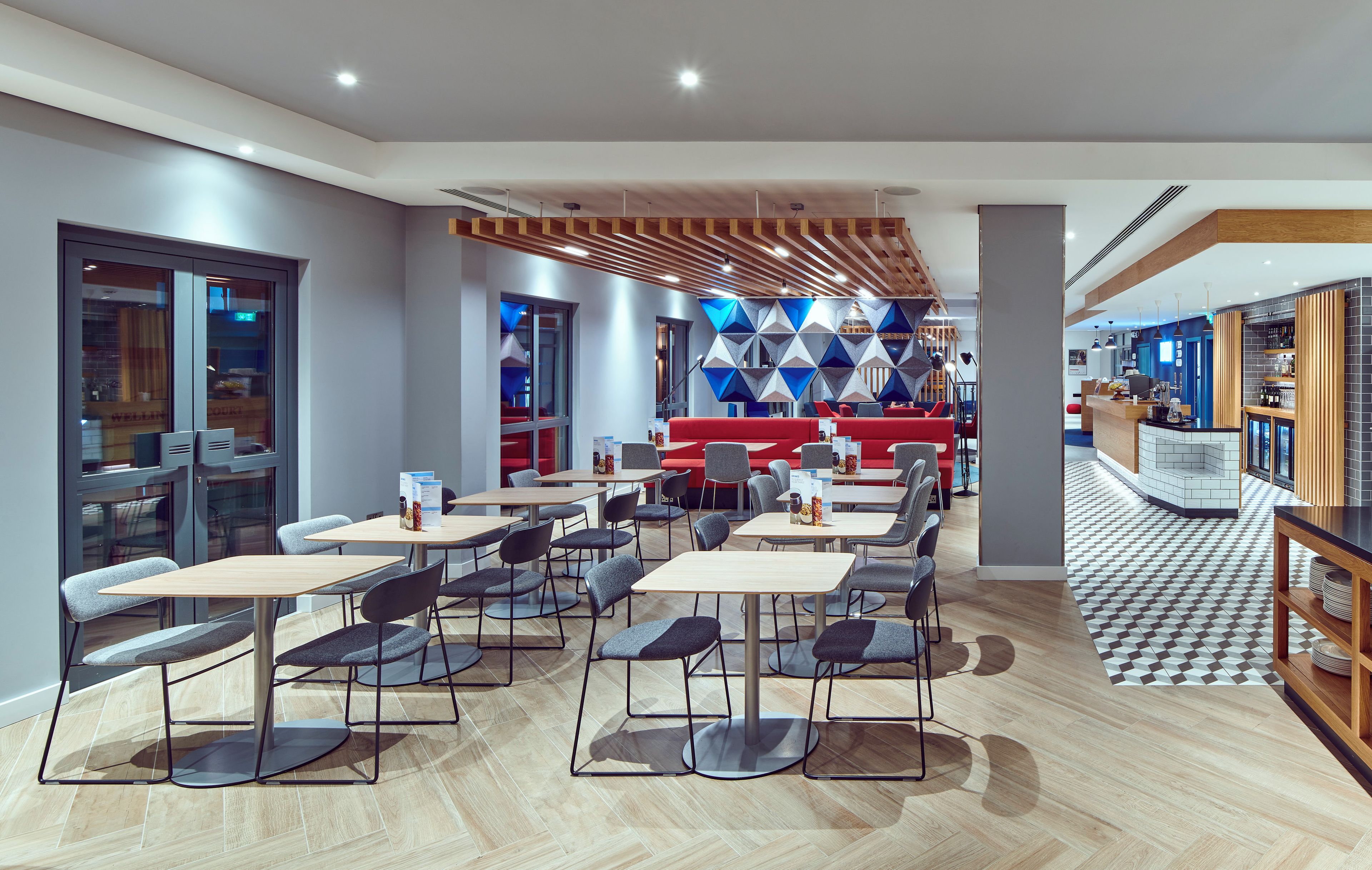 A modern restaurant with multiple tables and chairs, a bar area, and a patterned wall design.