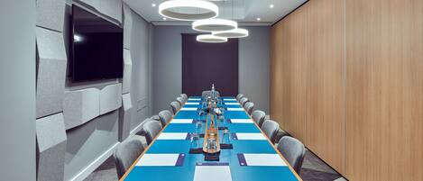 A conference room with a long table, chairs, a flat-screen TV, and modern lighting fixtures.