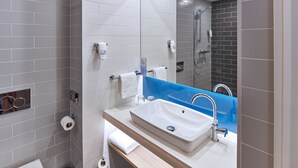 A modern bathroom with a white sink, a mirror, and a shower area.