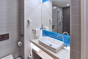 A modern bathroom with a white sink, a mirror, and a shower area.