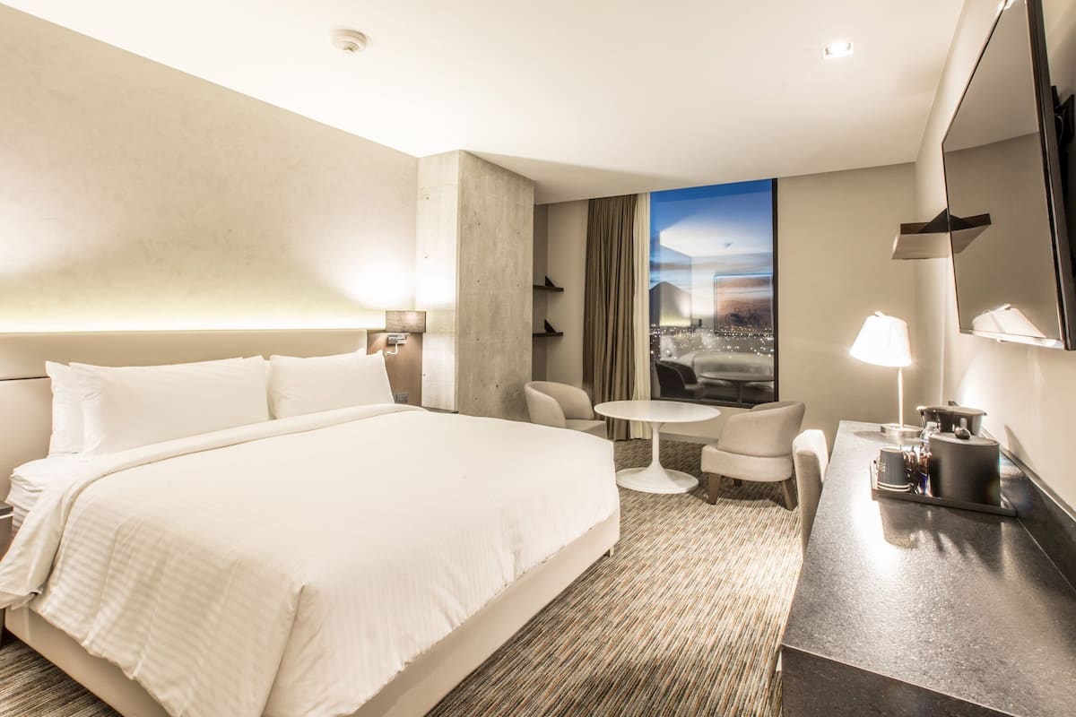 A modern hotel room with a large bed, a small round table, a sofa, and a TV.
