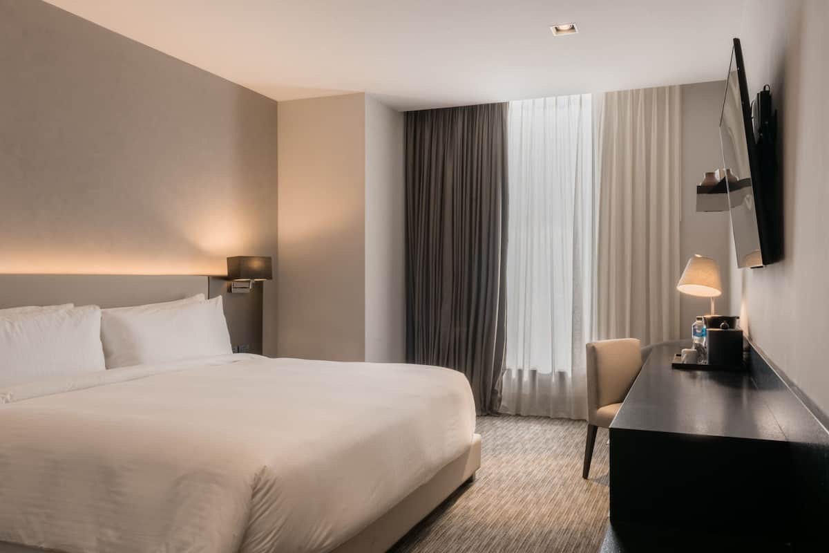 A hotel room with a large bed, a desk with a lamp, a chair, and a TV mounted on the wall.