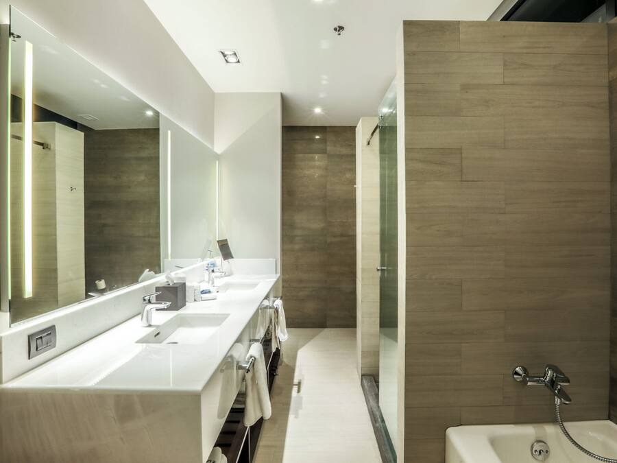 Un baño moderno con un espejo grande, dos lavamanos, una ducha y una bañera.