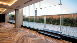 Un interior amplio con piso de madera en espiga, ventanas grandes y vista a una pared de ladrillo y plantas al exterior.