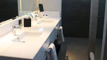 Un baño moderno con tres lavamanos, un espejo grande y una cabina de ducha de vidrio.
