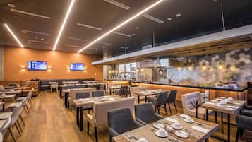 A modern restaurant with multiple dining areas, a kitchen visible in the background, and digital menu displays on the wall.