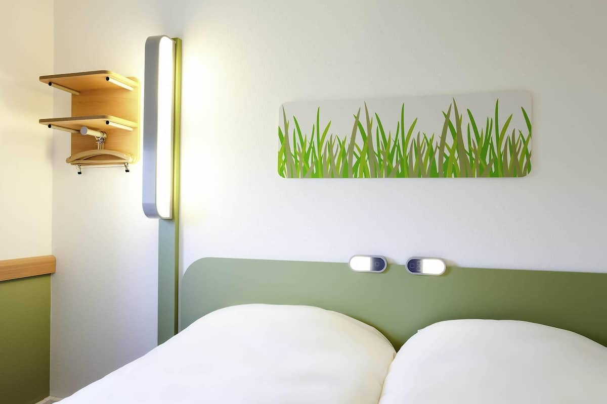 Ein Bett mit zwei Kissen, einer Wandleuchte und einem Kunstwerk mit Grasmuster.