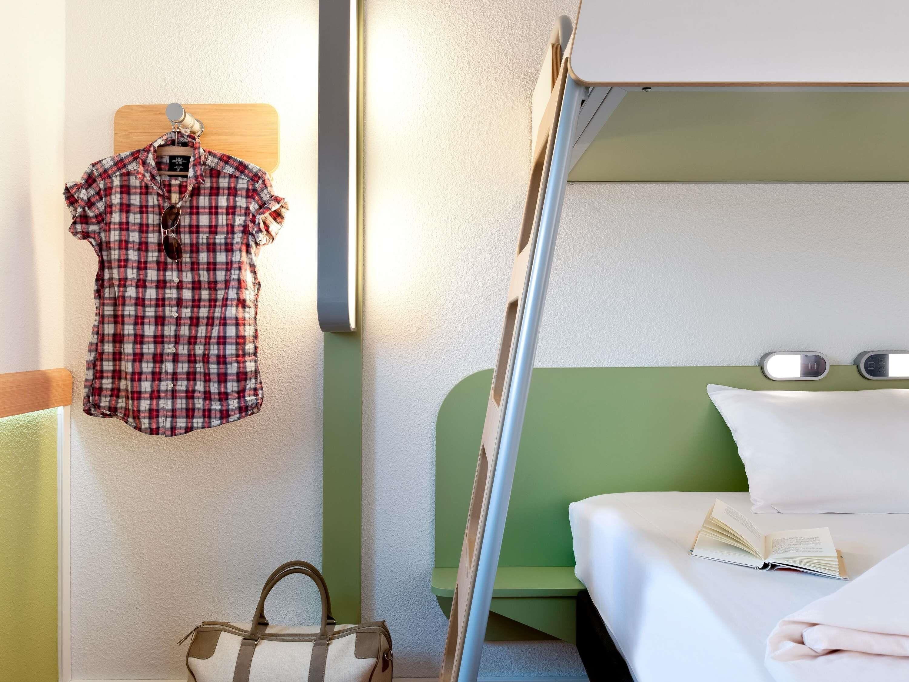 Una cama litera con cabecera verde, una camisa colgada, un bolso de mano y un libro sobre la cama.