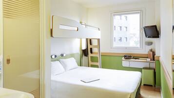 A hotel room with a bunk bed, a desk with a computer, a window, and a bathroom.