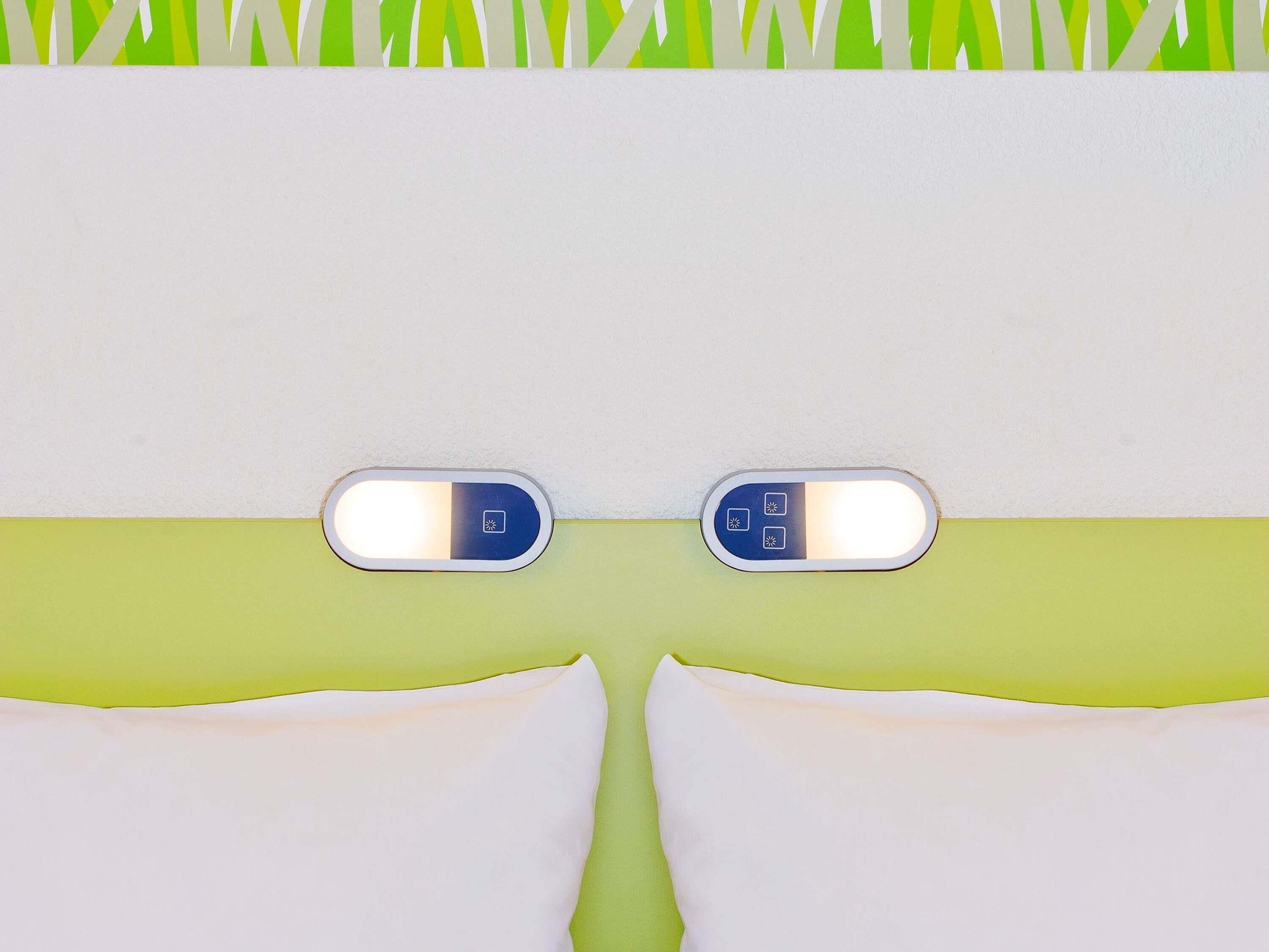 A bathroom with a white sink, two illuminated mirrors, and a green wall.